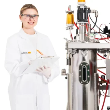 Technician taking notes beside an Infors Techfors-S 2 stainless steel bioreactor